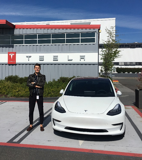 Remi Koch stands beside a car in the Tesla parking lot.