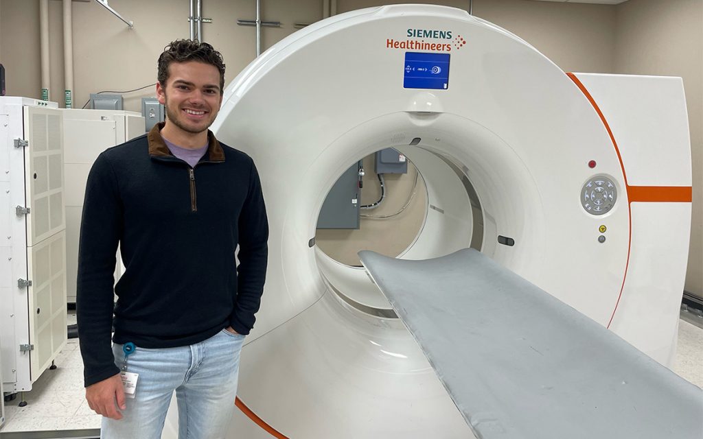 Camden Shuman stands next to an MRI machine at Siemans Healthineers.