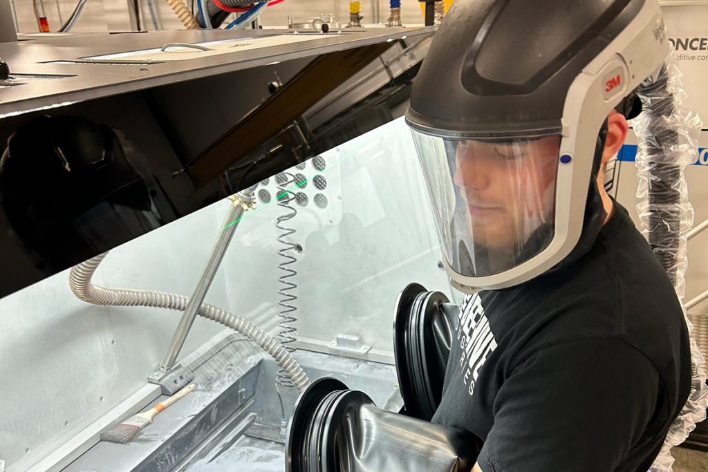 Zachary Koller wearing a respiratory mask and other personal protective equipment while working in a controlled environment within an enclosed piece of machinery.